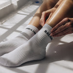 White grip socks with text worn by a person sitting on a light-colored surface.