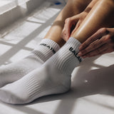 White grip socks with text worn by a person sitting on a light-colored surface.