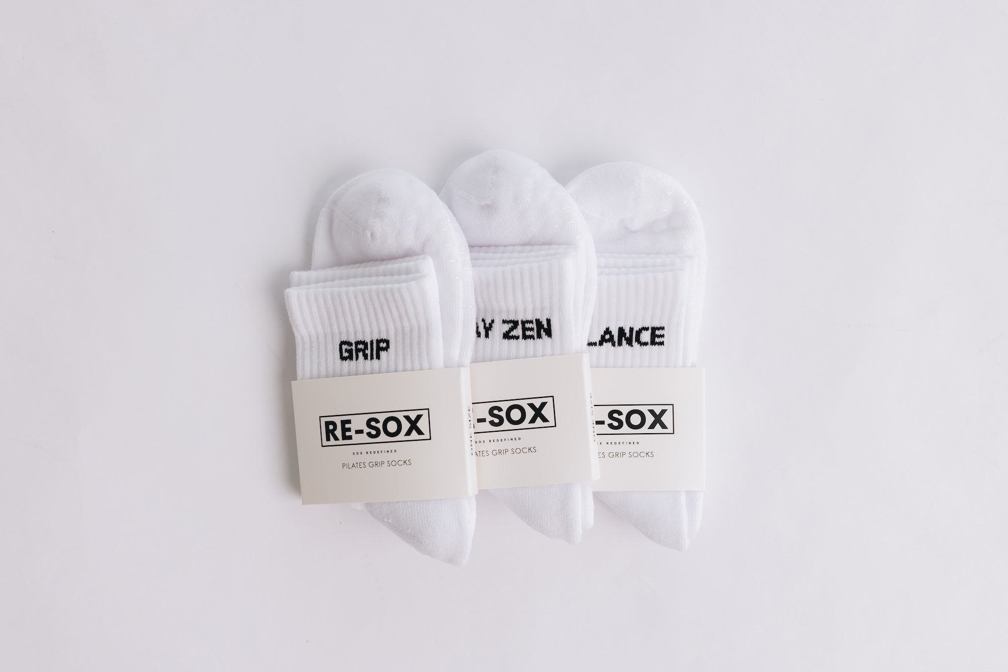 Three white ribbed pairs of grip socks featuring slogans Breathe/Balance, Stay Zen and Grip & Go. packaged with RE-SOX sock card. 
