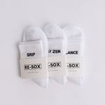 Three white ribbed pairs of grip socks featuring slogans Breathe/Balance, Stay Zen and Grip & Go. packaged with RE-SOX sock card. 