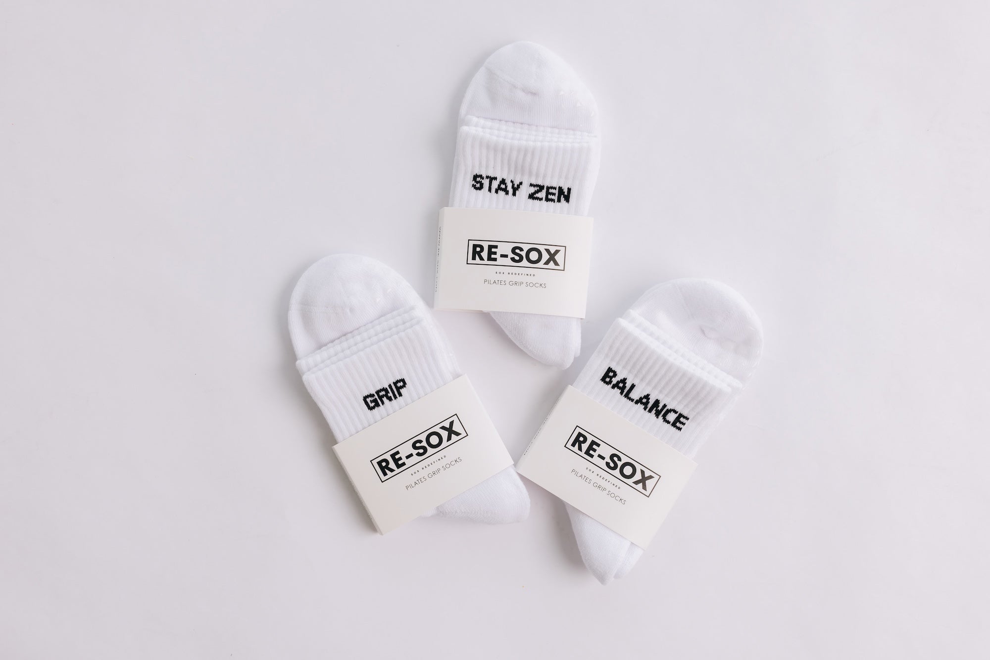 Three white ribbed pairs of grip socks featuring slogans Breathe/Balance, Stay Zen and Grip & Go packaged in RE-SOX sock card. 