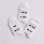 Three white ribbed pairs of grip socks featuring slogans Breathe/Balance, Stay Zen and Grip & Go packaged in RE-SOX sock card. 