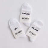 Three white ribbed pairs of grip socks featuring slogans Breathe/Balance, Stay Zen and Grip & Go packaged in RE-SOX sock card. 