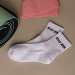 White grip socks with 'Stay Zen' text on a beige surface, next to a pink fabric and green yoga mat.
