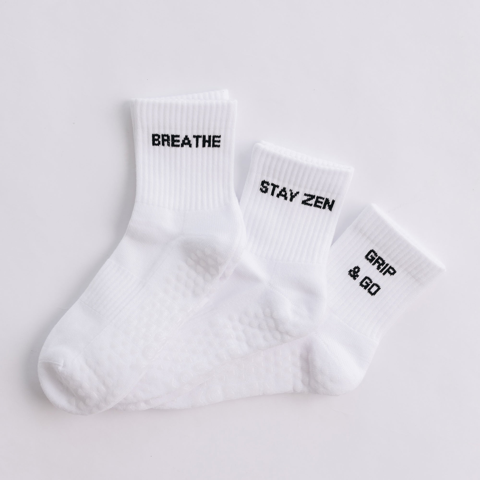 Three white ribbed pairs of grip socks featuring slogans Breathe/Balance, Stay Zen and Grip & Go
