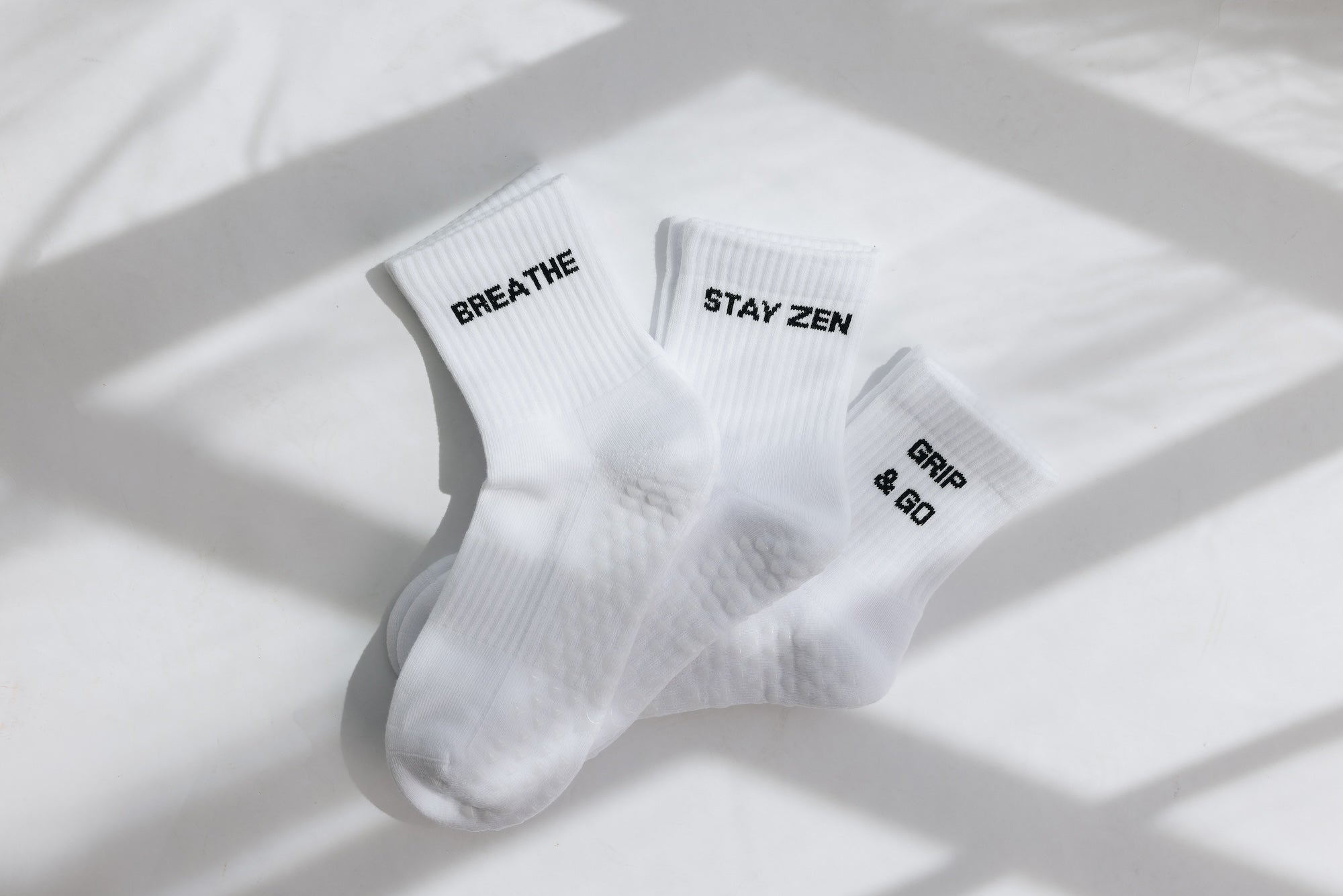 Three white ribbed pairs of grip socks featuring slogans Breathe/Balance, Stay Zen and Grip & Go