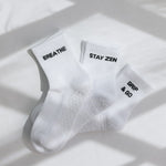 Three white ribbed pairs of grip socks featuring slogans Breathe/Balance, Stay Zen and Grip & Go