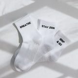 Three white ribbed pairs of grip socks featuring slogans Breathe/Balance, Stay Zen and Grip & Go