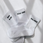 Three white ribbed pairs of grip socks featuring slogans Breathe/Balance, Stay Zen and Grip & Go