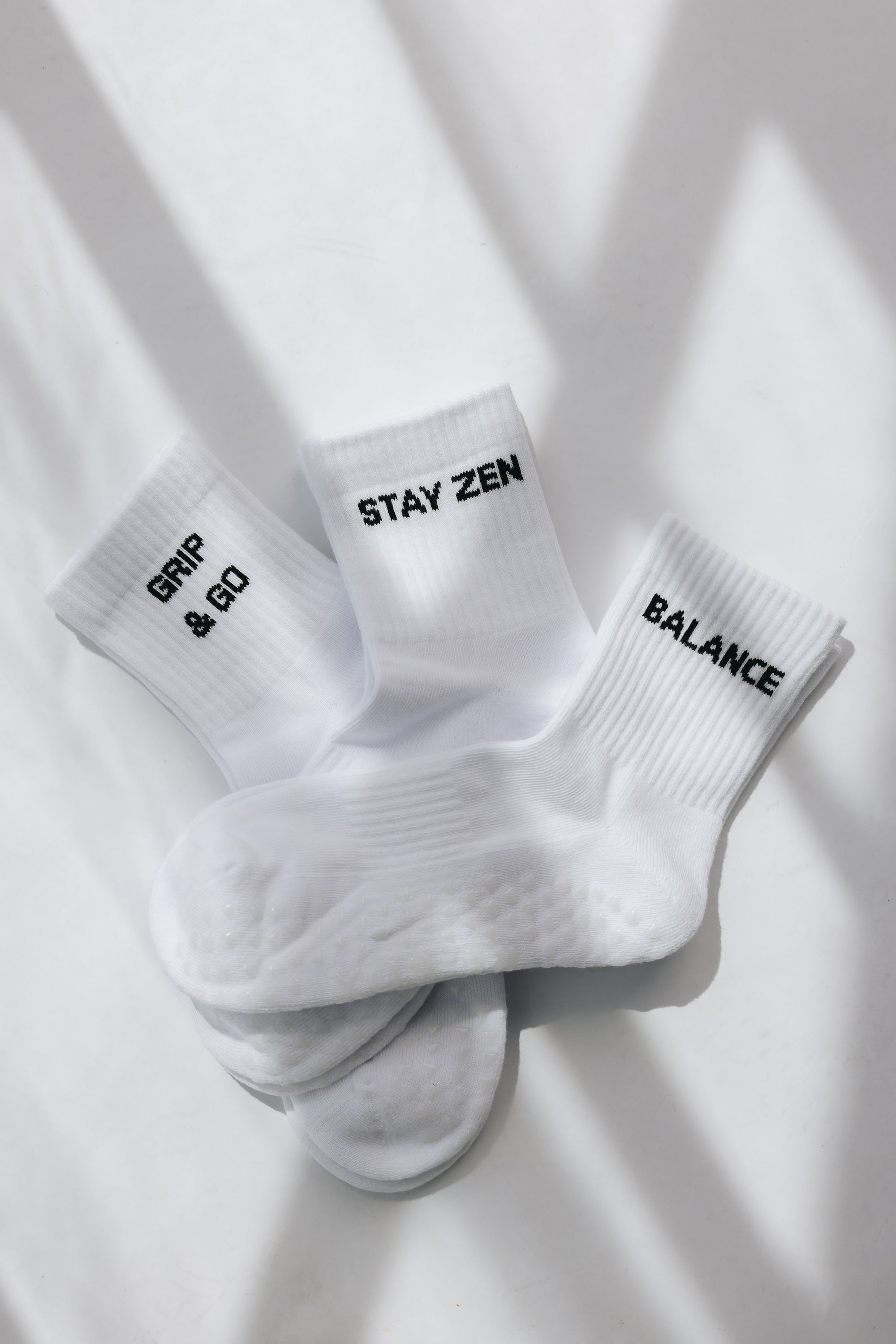 Three white ribbed pairs of grip socks featuring slogans Breathe/Balance, Stay Zen and Grip & Go