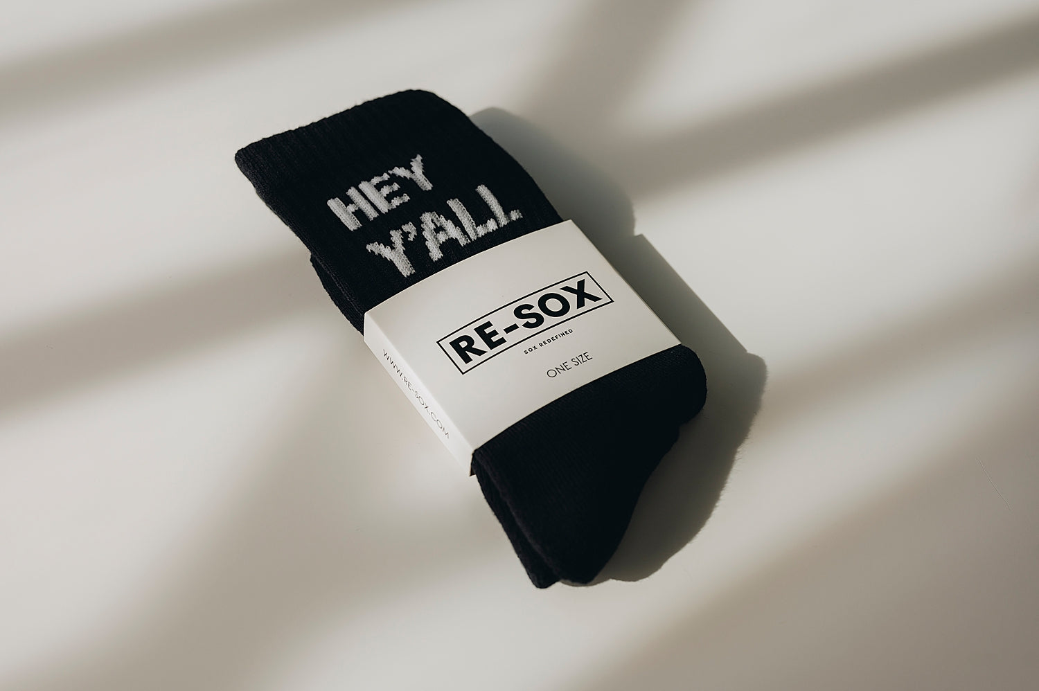 A pair of black ribbed crew socks with the text 'HEY Y'ALL' printed on the side, shown in packaging, a white card with RE-SOX logo. 